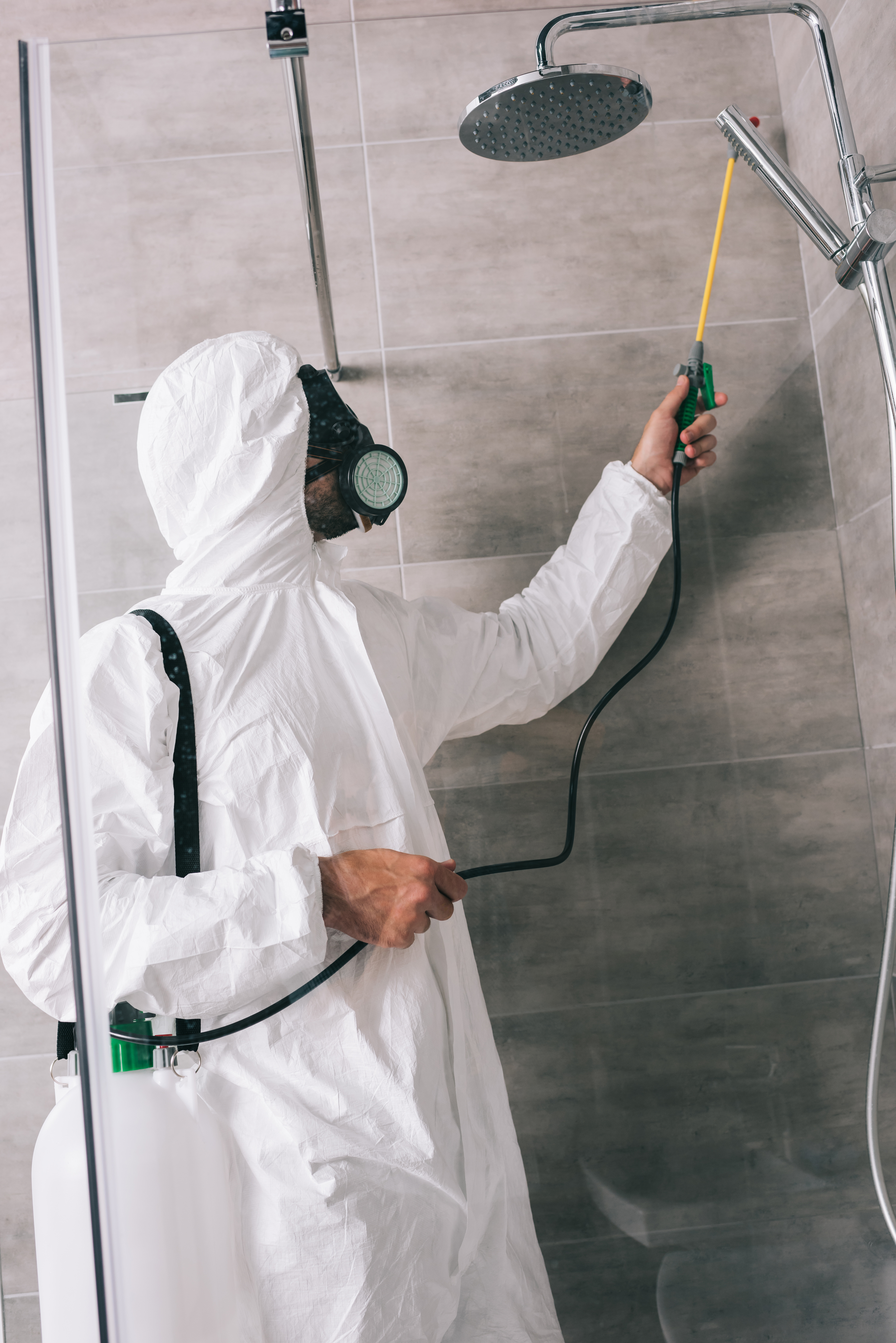 side view of pest control worker spraying pesticides with sprayer in bathroom