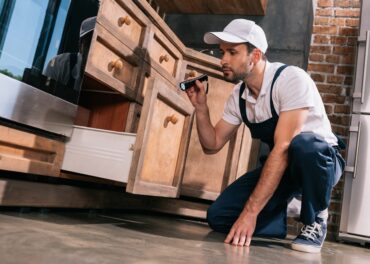 pest control worker examining kitchen with flashlight